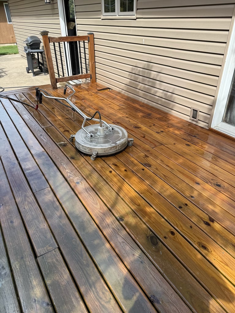 Wooden deck with surface cleaner equipment, wooden chair, and house siding visible in background