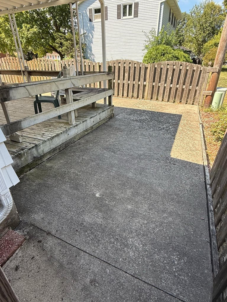 Backyard patio area with concrete ground, wooden picnic table, pergola, fenced yard, and white residential house