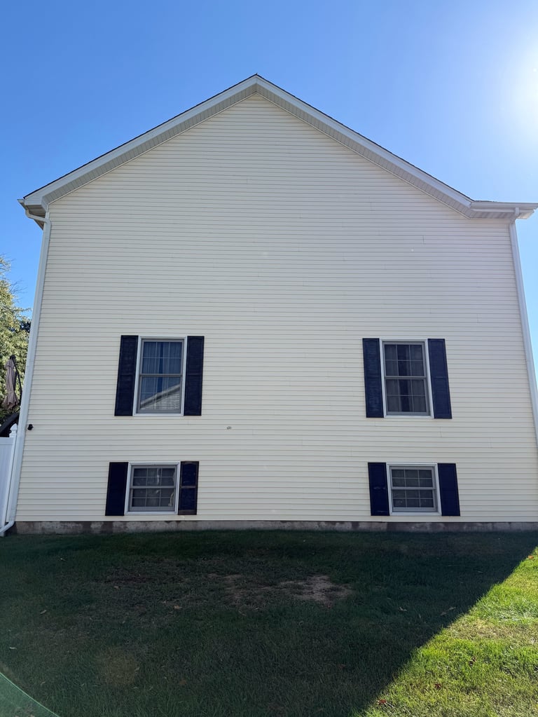 White two-story house with black shutters and four windows under clear blue sky