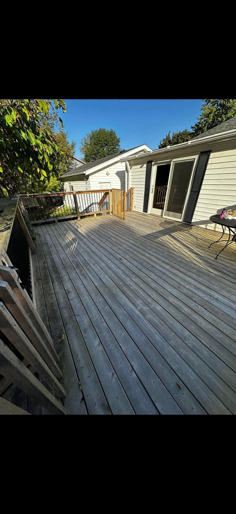 Spacious wooden deck attached to a modern house with railings, overlooking landscaped yard on a clear sunny day