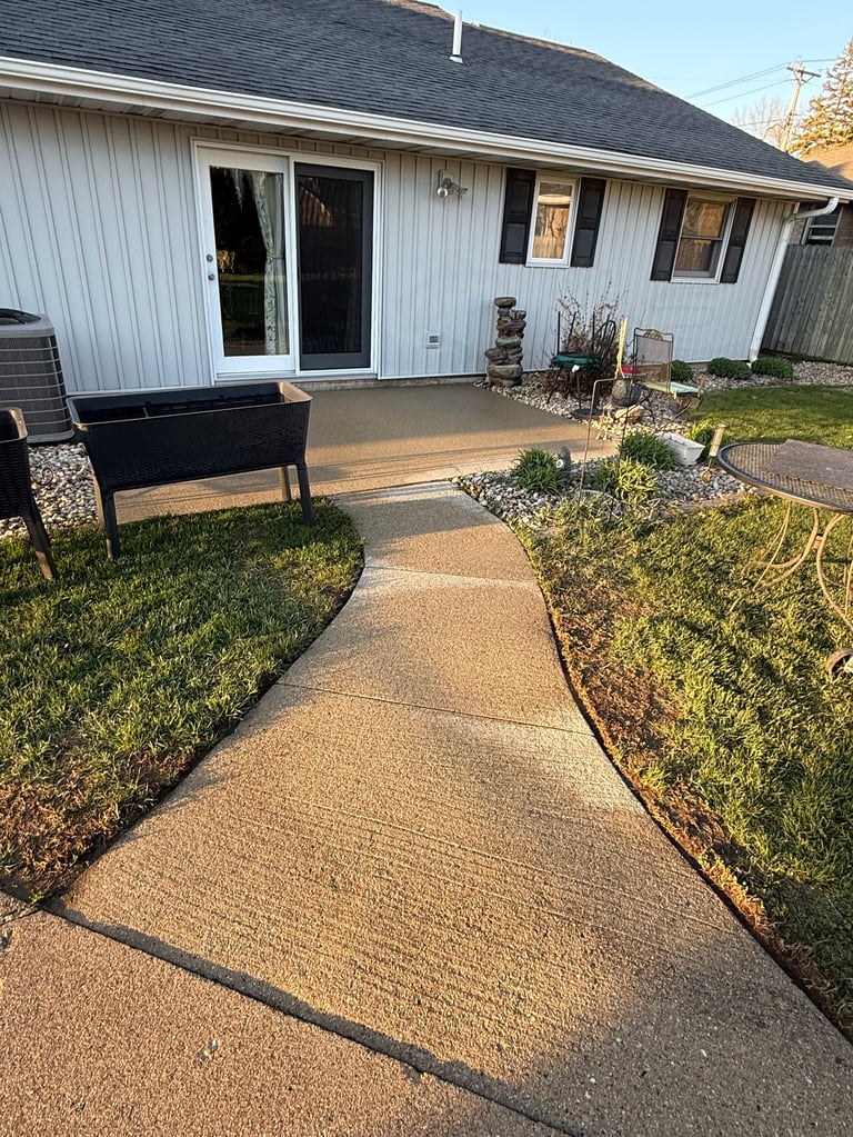 White house with dark roof and multiple doors, concrete patio area with black bench and landscaping along pathway