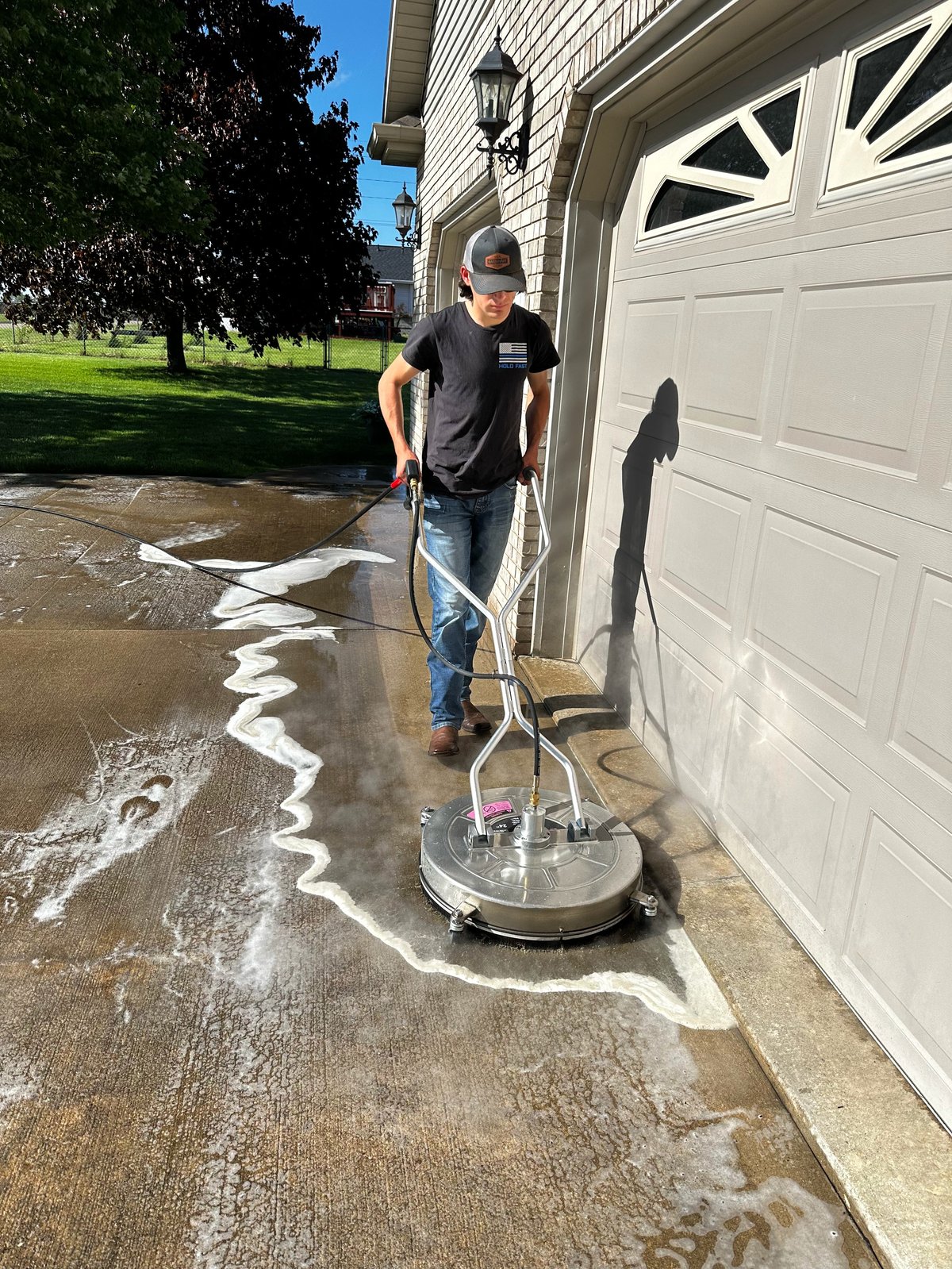 Man using pressure washer to clean concrete driveway with soapy water and white cleaning solution markings visible