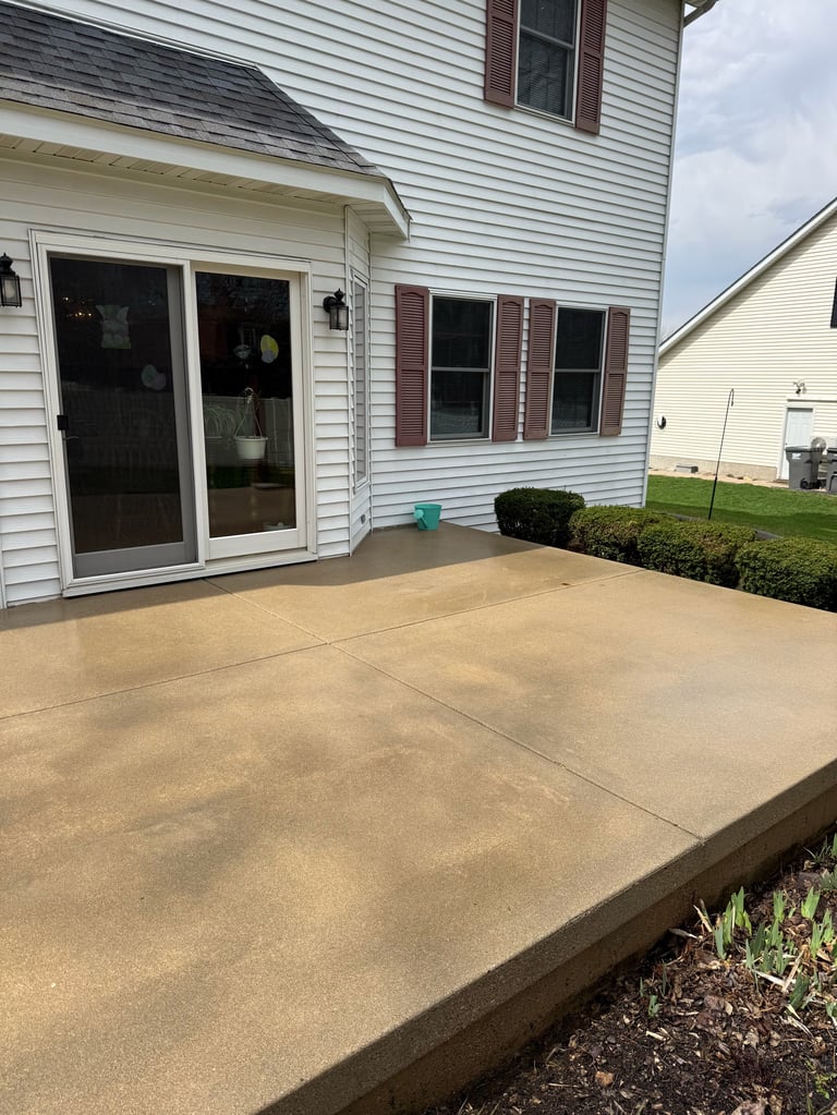 Concrete patio extending from a white two-story house with glass doors and shrubs nearby