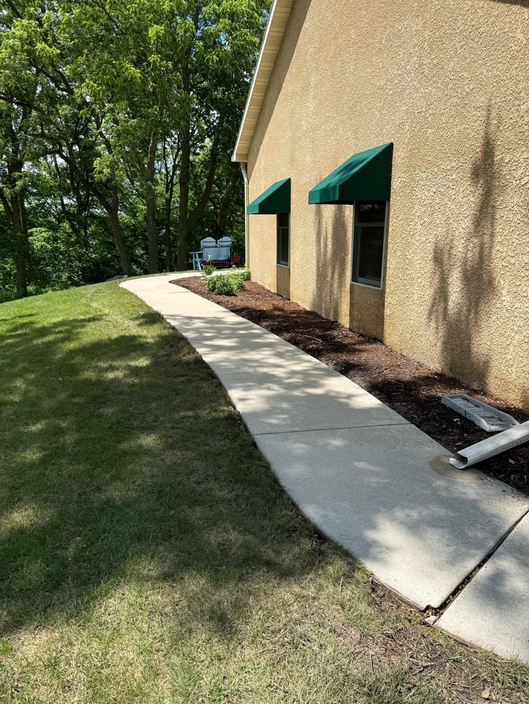Exterior of beige building with green awnings, concrete walkway, manicured lawn, and trees in background