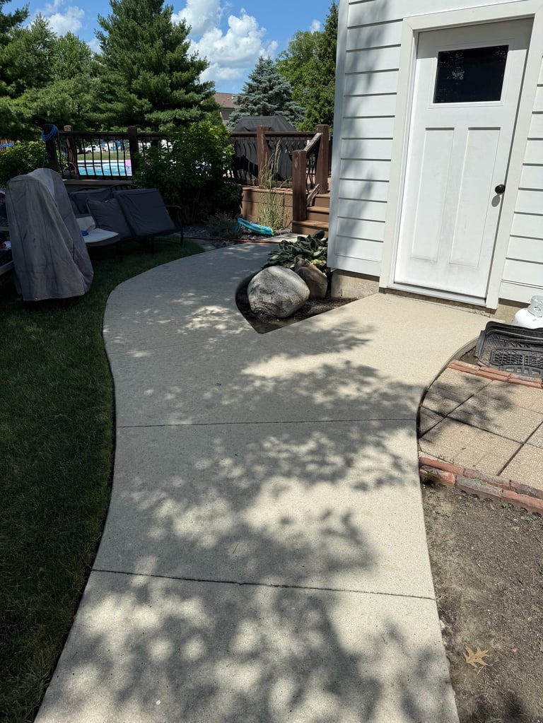 Concrete patio pathway in backyard with white storage shed, lounge chairs, and trees under blue sky