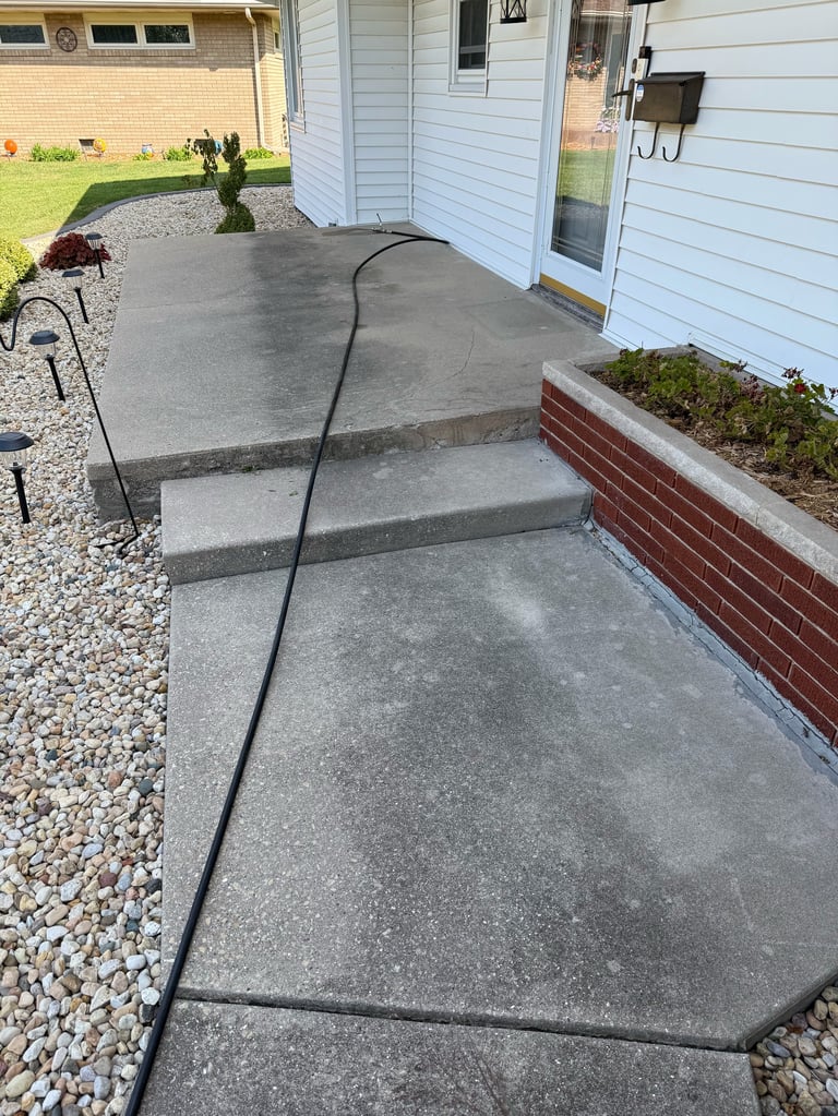 Concrete patio with black extension cord and steps leading to white residential home