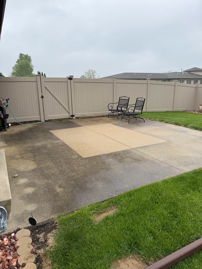 Backyard patio with two lounge chairs on concrete pad, metal fence, and green lawn bordered by landscaping