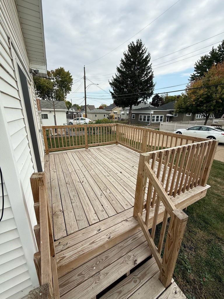 Wooden deck with railings attached to white house, suburban street visible in background