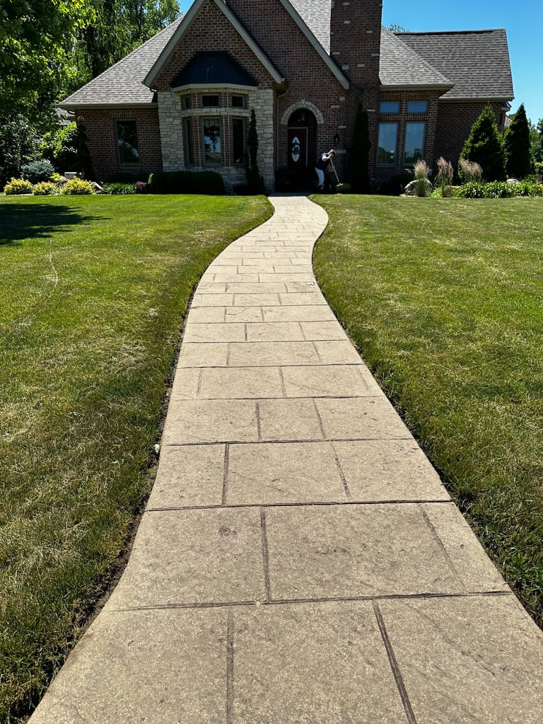 Curved concrete pathway leading to a brick two-story house with manicured lawn on a sunny day