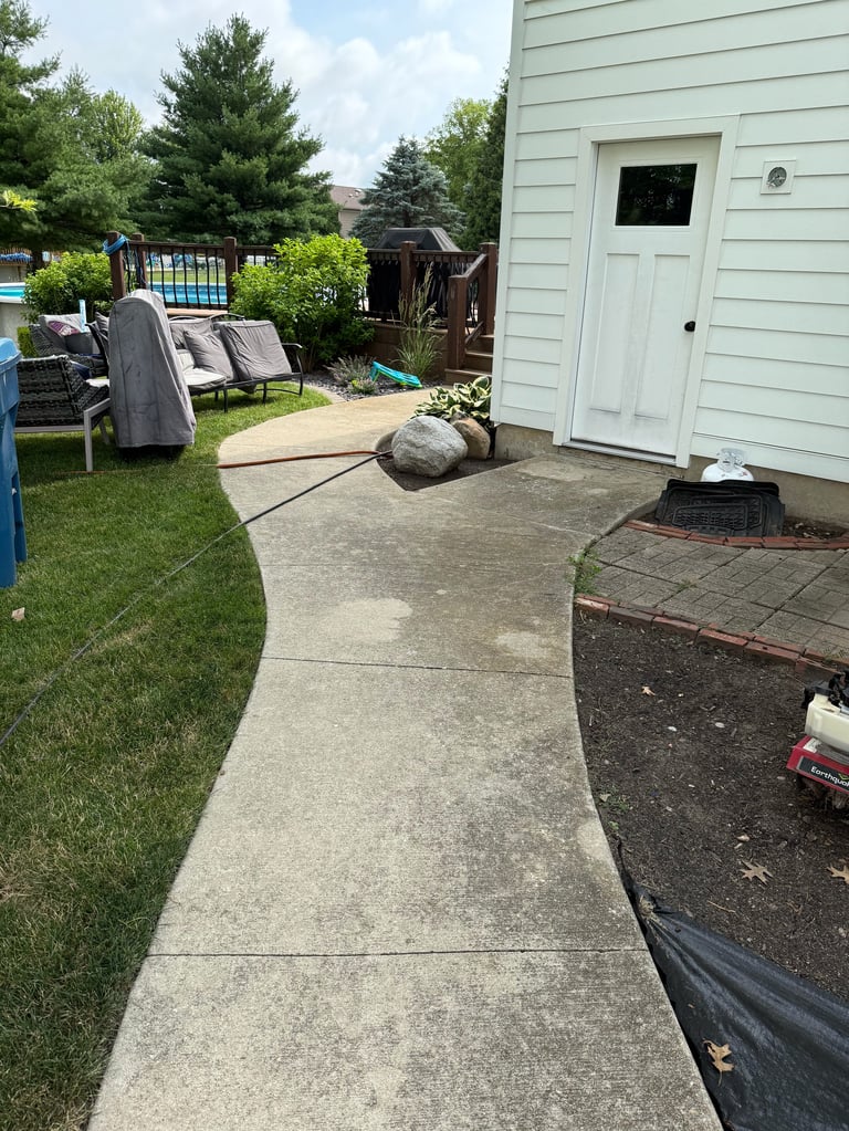 Backyard patio with concrete pathway leading to white shed, lawn furniture, pool gate, and landscaping