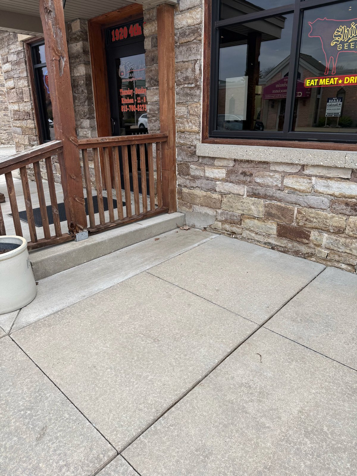 Storefront entrance with wooden gate, concrete patio, and brick building facade with windows and neon signage