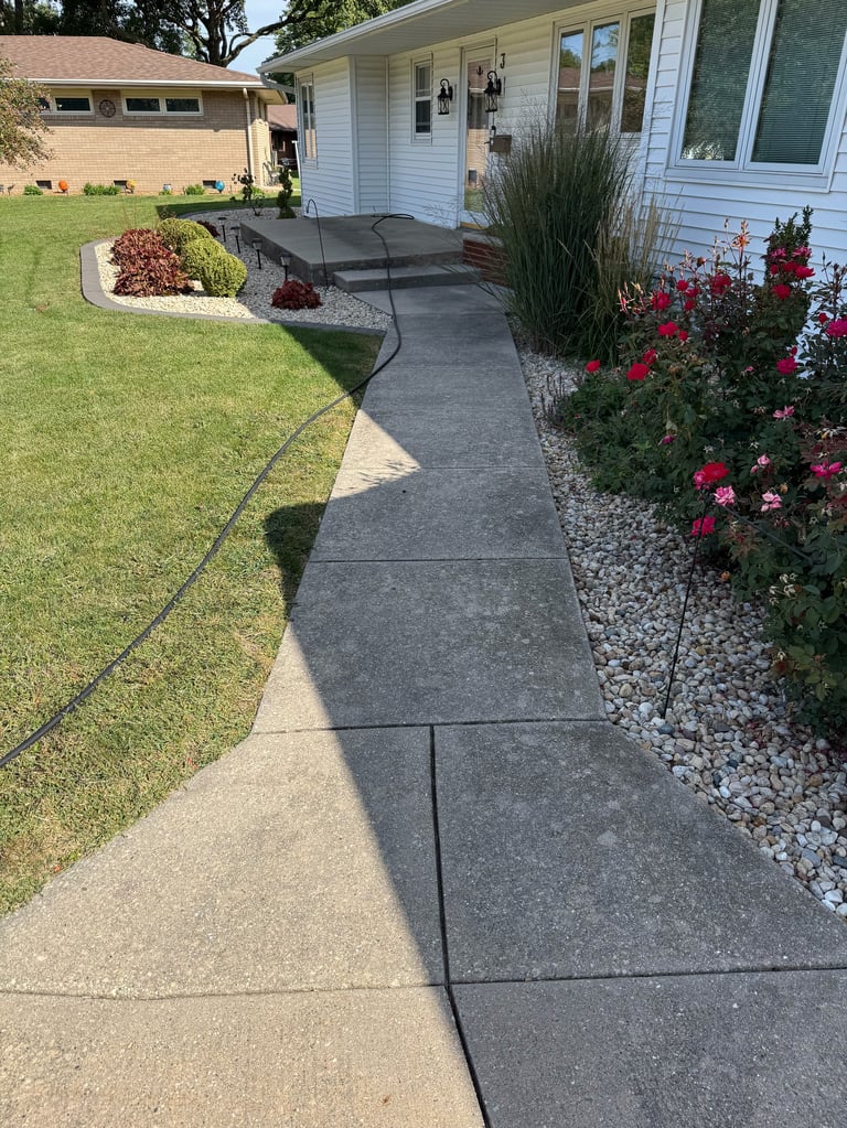 Front entrance of a mid-century modern home with a concrete walkway leading to the door, flanked by green lawn on the left and red flowers with gravel landscaping on the right