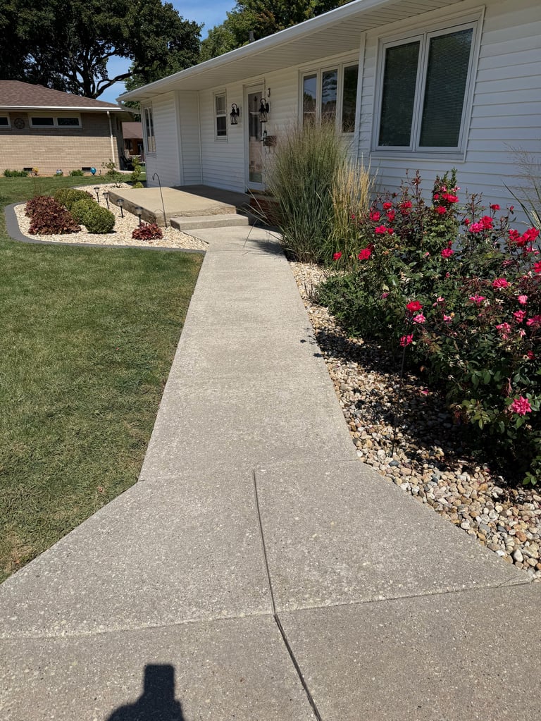 Modern white ranch home with concrete sidewalk, red flowering shrubs, ornamental grass, and manicured lawn on sunny day
