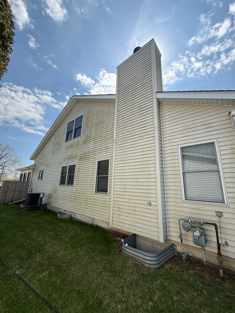 White sided two-story house with vertical chimney viewed from the backyard on a sunny day with blue sky