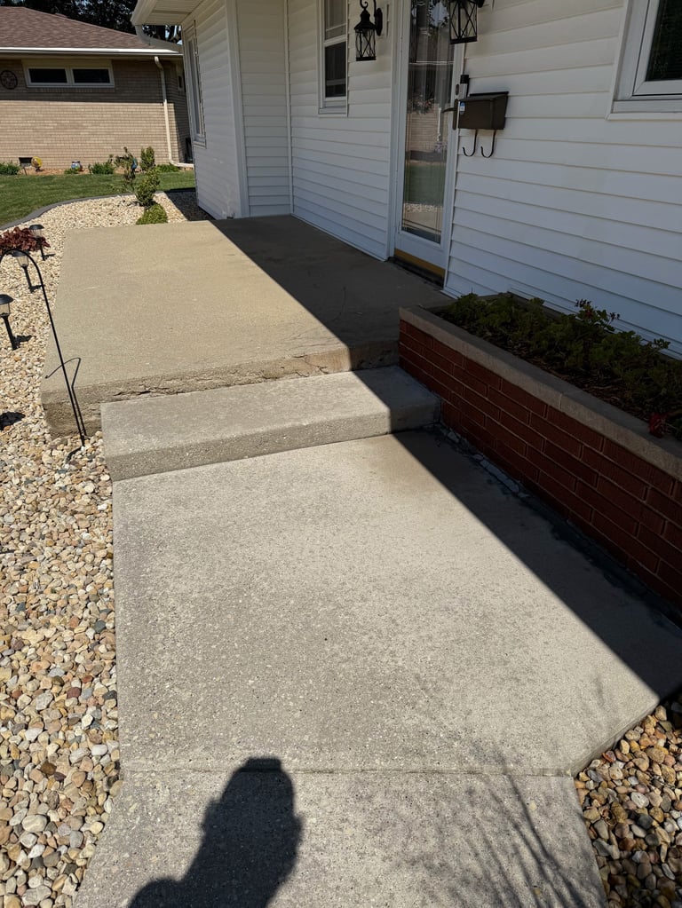 Concrete walkway leading to white residential house with brick foundation and gravel borders