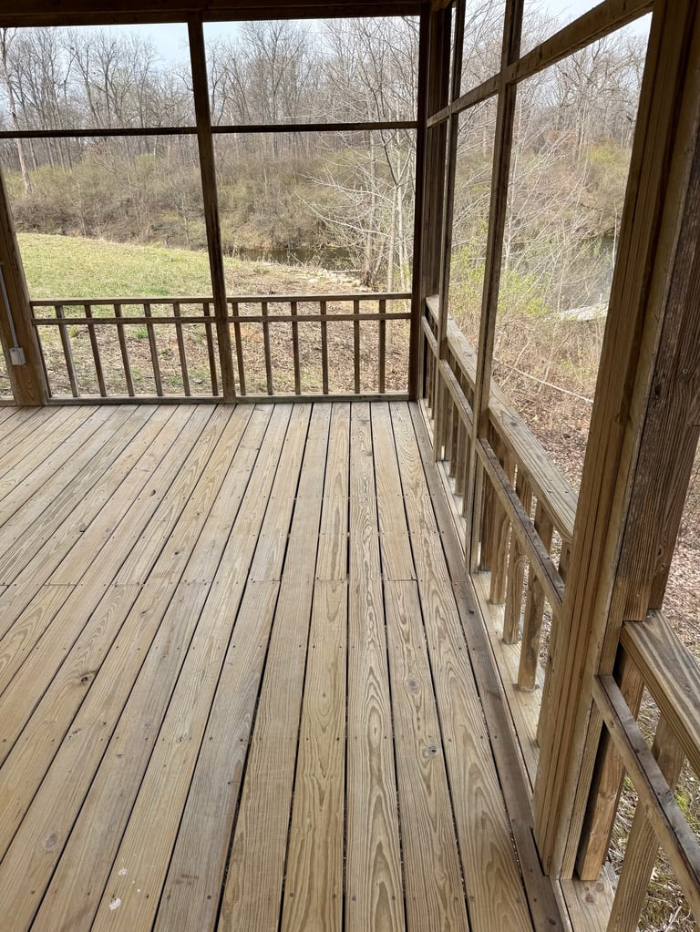 Empty wooden deck with railing overlooking bare trees and grassy landscape during early spring